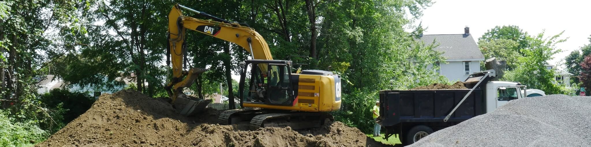 Four Seasons Property Maintenance excavator on a residential construction site with a large dirt pile in Western Massachusetts