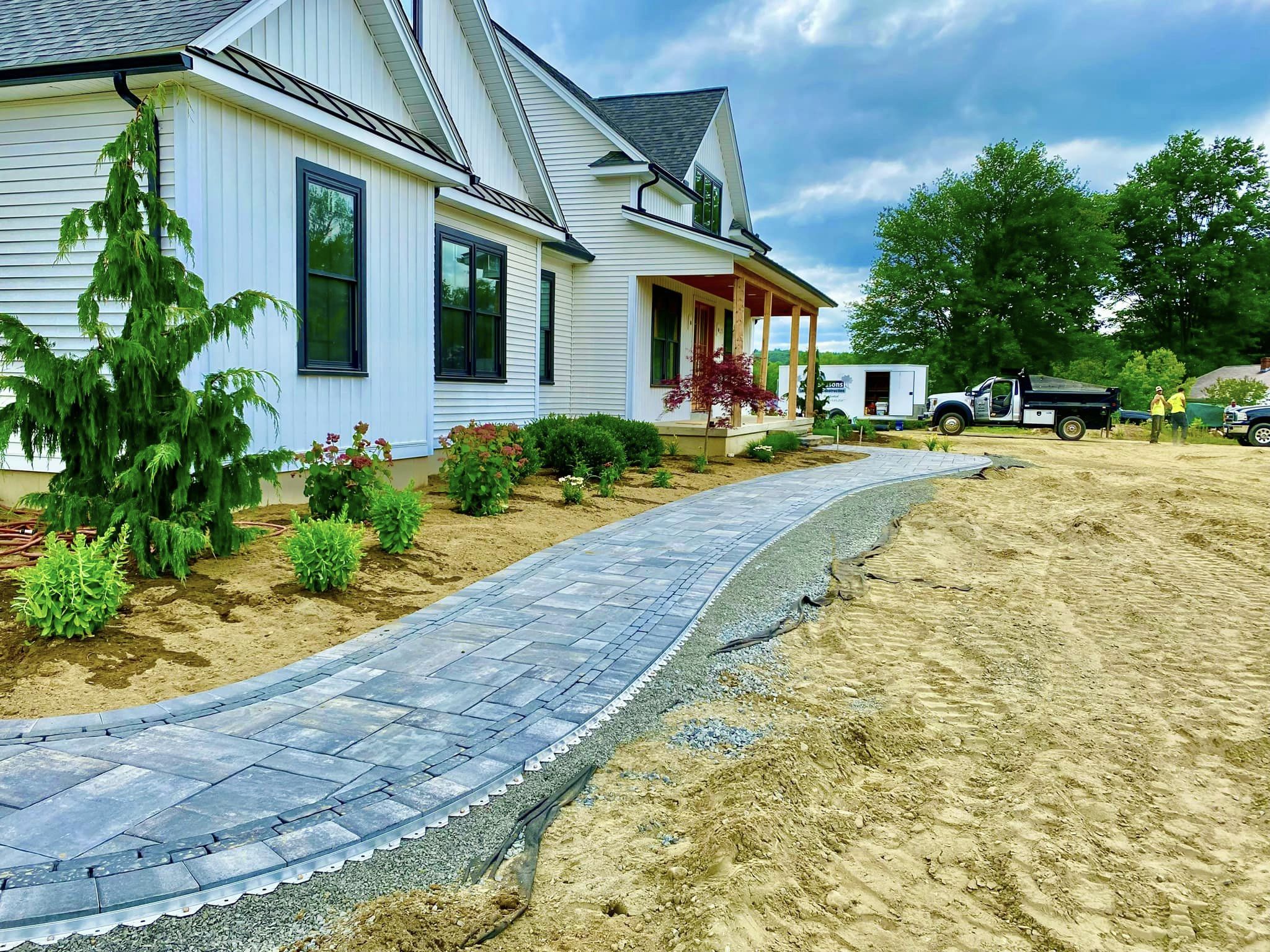 Newly installed curved paver walkway leading to a modern farmhouse style home with landscaping beds in Western Massachusetts