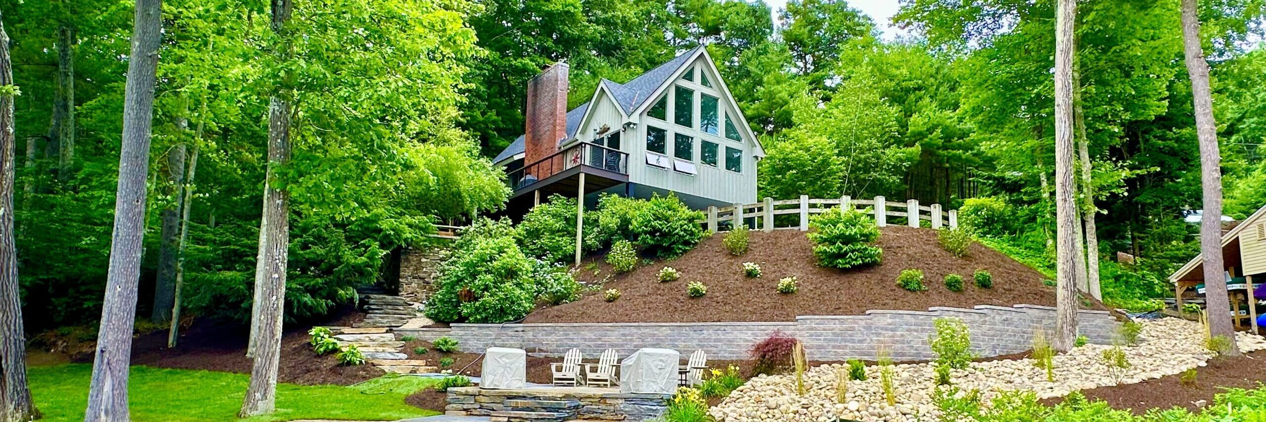Tiered stone retaining walls with landscaping beds and outdoor seating area on a lakefront property in Western Massachusetts
